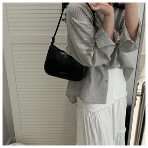 Detail of minimalist black leather underarm bag featuring silver fashion text logo