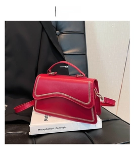Detail of red square handbag with gold stitching and thick handle on white props
