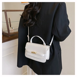 Detailed view of white crossbody bag with gold lock worn over a black blazer