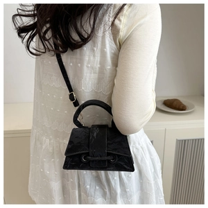 Mini trapezoid handbag in black wrinkled texture shown as a stylish crossbody on a model