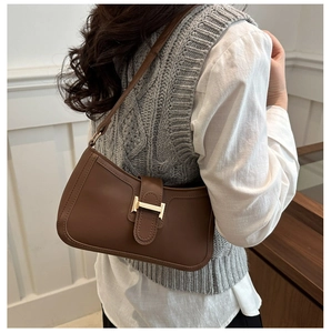 Sac à épaule chic en cuir marron avec boucle dorée porté par un mannequin dans un intérieur