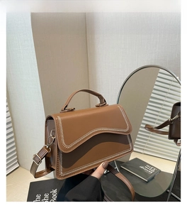Brown leather shoulder bag with wavy flap design and beige contrast stitching detail