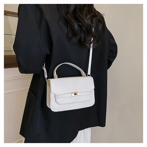 Macro detail of the golden metallic twist lock on a white leather minimalist handbag
