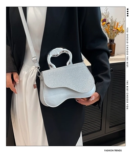 Detail of silver saddle bag featuring sequin flap and unique sculptural metal handle