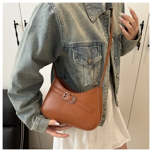 Close-up of caramel leather underarm bag with decorative metal buckle and slim strap
