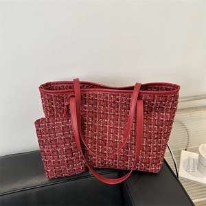 Red tweed tote bag with matching pouch and red leather handles on a black sofa