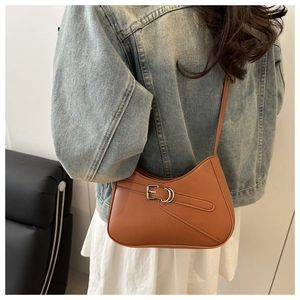 Side view of tan leather underarm bag with silver buckle strap shown on a model