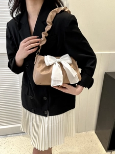 Close-up of khaki pleated handbag featuring a large white bow and matching wide strap