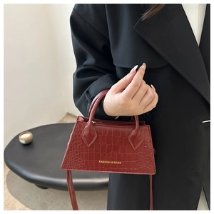 Close-up of burgundy crocodile pattern handbag with gold fashion logo and top handle