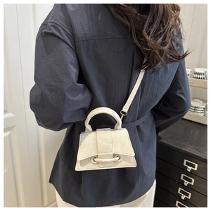 Model view showing the back side of a beige trapezoid mini handbag with crossbody strap