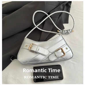 Close-up of silver metallic shoulder bag with gold buckles next to a smartphone for scale