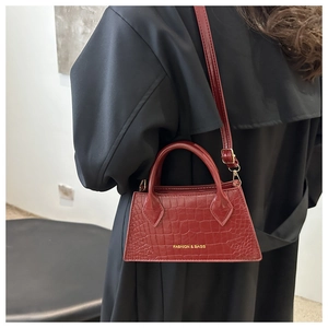 Detail of burgundy crocodile pattern leather handbag with gold logo and top handle