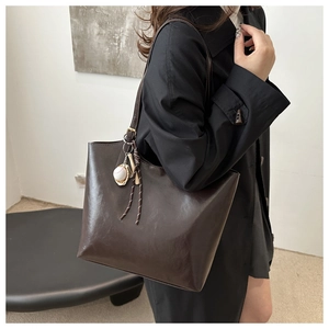 Detail of dark brown leather tote with a baseball charm and vintage metal hardware