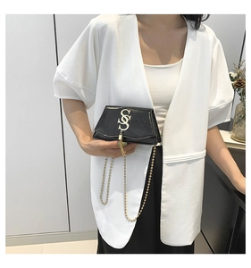 Détail d'un sac en cuir verni noir avec logo doré en S et bandoulière en chaîne