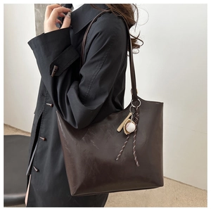 Detail of soft brown leather tote bag with a unique baseball bat charm accessory