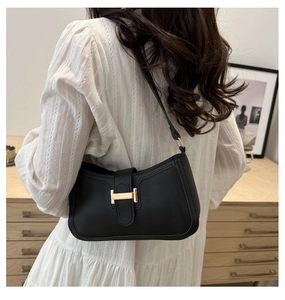 Détail du sac hobo noir avec fermoir H doré porté sur une robe blanche élégante