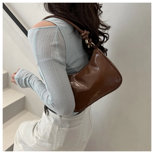 Detailed view of brown leather shoulder bag with decorative strap knot and metal ring