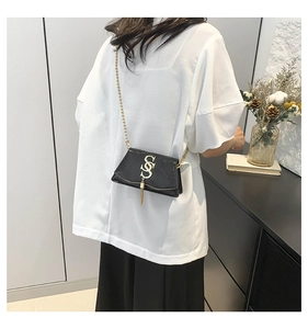 Détail d'un mini sac noir brillant avec bandoulière chaîne dorée et gland en métal