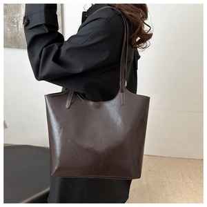 Detail of a large vintage dark brown leather tote bag worn by a model in a minimalist setting