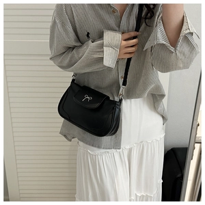 Chic black leather semi-circle crossbody bag with silver bow detail on a stylish model