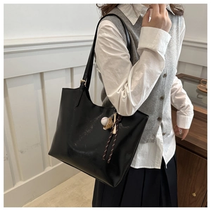 Close-up of black leather tote bag with unique baseball theme charms and slim shoulder straps