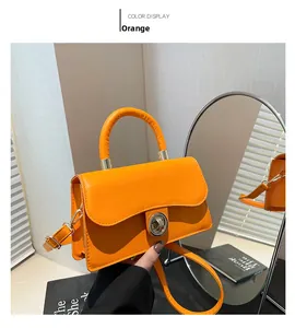Détail du sac à main orange avec fermoir rotatif en métal et poignée incurvée sous lumière douce