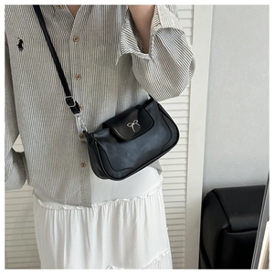 Detail of a vintage black crossbody bag with a silver bow accent and adjustable strap