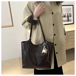 Detail of dark brown leather tote bag with baseball charm and sleek minimalist shoulder straps