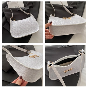 Macro details of white embossed underarm bag with gold bow and smooth zipper closure