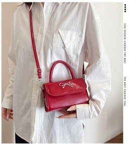 Side view of model carrying a glossy red crossbody bag with silver metal bow detail
