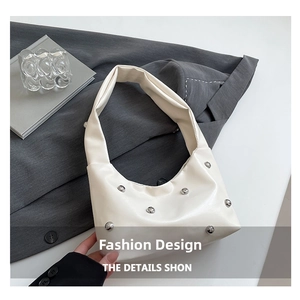Close-up of beige rivet hobo bag with silver studs on a neutral textured background