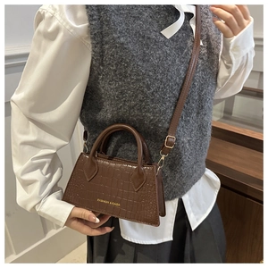 Detail of dark brown crocodile texture crossbody bag with gold fashion lettering