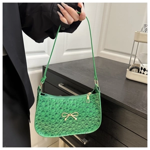 Détail du sac hobo vert embossé avec nœud doré tenu par un mannequin en main