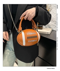 Close-up of orange football shaped crossbody bag with gold chain and letter embossing