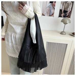 Detail of black large capacity shoulder bag with flowing fringes and lychee leather texture