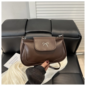 Close-up of brown leather handbag with silver bow metal buckle and curved flap detail