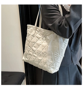 Détail d'un sac cabas matelassé blanc avec dentelle et nœud porté sur un blazer gris