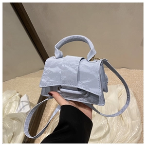 Detailed view of lilac mini handbag with pleated texture and round handle on white fabric