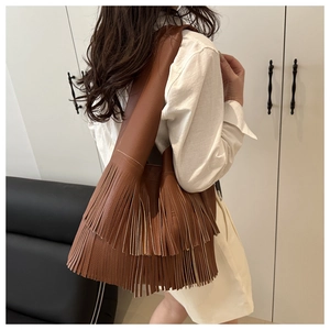 Detail of dark brown leather tote bag featuring dense bohemian fringes and pebble texture