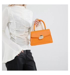Detail of orange handbag showing crocodile pattern leather and silver metal clasp
