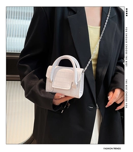 Detail of white crocodile texture mini bag with top handle and silver metal chain