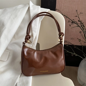 Brown glossy underarm bag with knot handle and gold hardware on white blazer