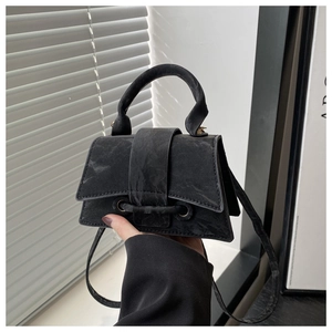 Detail of a black trapezoid crossbody bag with a matte texture and minimalist buckle