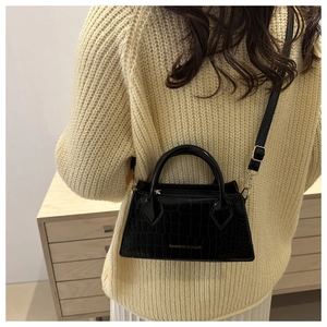 Detail of black crocodile pattern leather bag worn with a beige knitted sweater