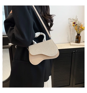 Detail of beige saddle bag featuring a glittery flap and unique silver metal handle