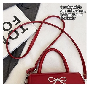 Detail of red patent leather handbag featuring a silver metal bow buckle and smooth texture