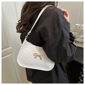 Detail of white embossed leather shoulder bag featuring a gold bow accent on a model