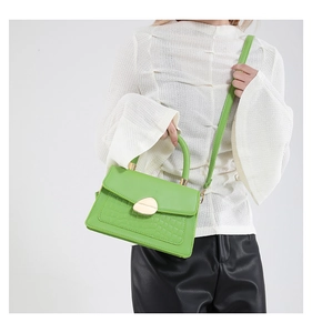 Détail du sac à main vert à motif crocodile avec fermoir doré sur tenue blanche