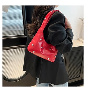 Detail of red faux leather underarm bag featuring glossy finish and silver stud rivets
