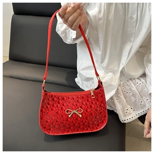 Close-up of red underarm bag with embossed dot texture and golden bow hardware